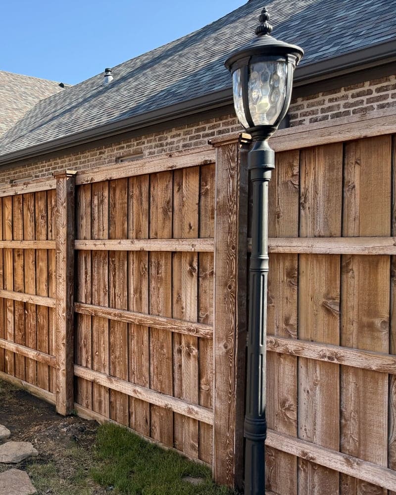 Side-yard wood privacy fence along a brick house, before staining